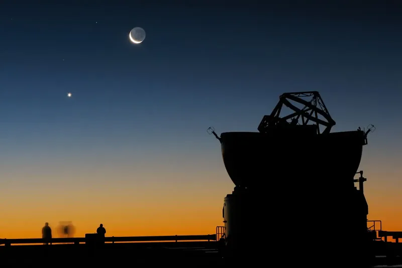 Un mince croissant de Lune et l’éclat de Vénus au-dessus de la silhouette d’un télescope
