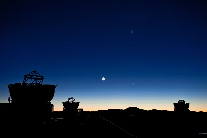 Vénus, Mercure, Jupiter, Mars et un fin croissant de Lune dans le ciel bleu de l’aube, au-dessus des télescopes de Paranal