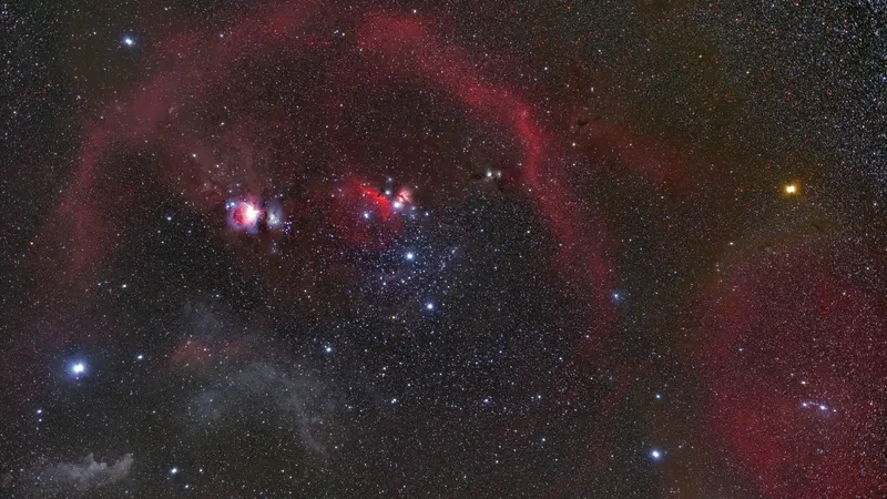 La constellation d’Orion, couchée sur le côté : Rigel bleue, Bételgeuse orangée, la ceinture et de grands arcs rouges