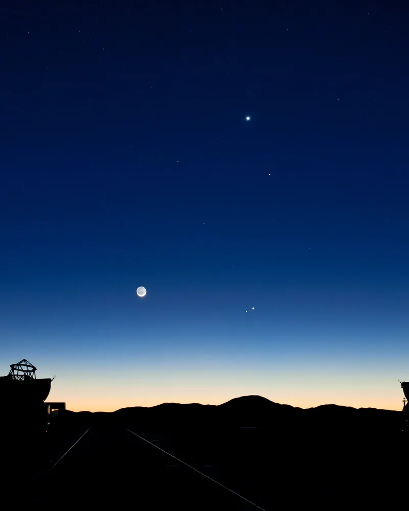 Vénus, Mercure, Jupiter, Mars et un fin croissant de Lune dans le ciel bleu de l’aube, au-dessus des télescopes de Paranal