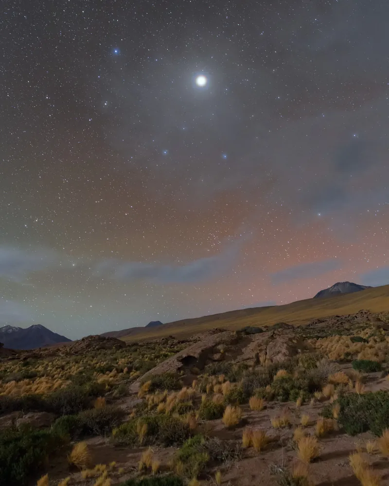 Jupiter, très brillante, entourée d’un halo, au-dessus du désert d’Atacama, sous un ciel étoilé aux lueurs rouges et vertes