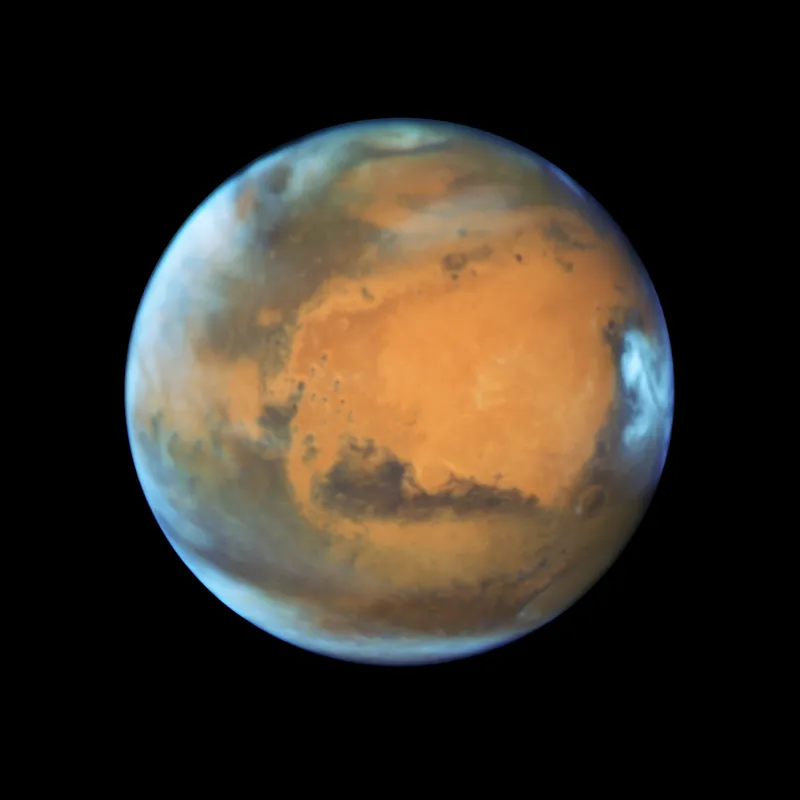 Mars en couleurs naturelles vue par Hubble en 2016 : plaines orangées, régions sombres et nuages blancs sur le bord