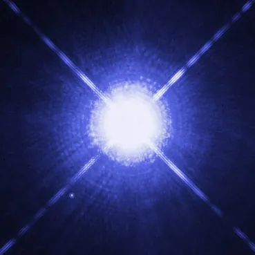 Sirius A surexposée, traversée de pointes en croix, et Sirius B, minuscule point en bas à gauche, vues par Hubble