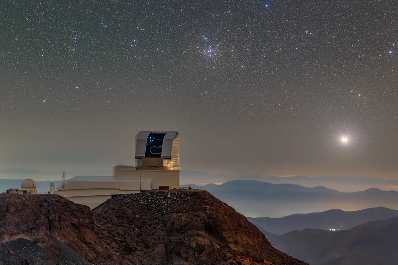 Sirius, point très brillant entouré d’un halo, bas sur l’horizon à droite de l’observatoire Vera C. Rubin, dôme ouvert