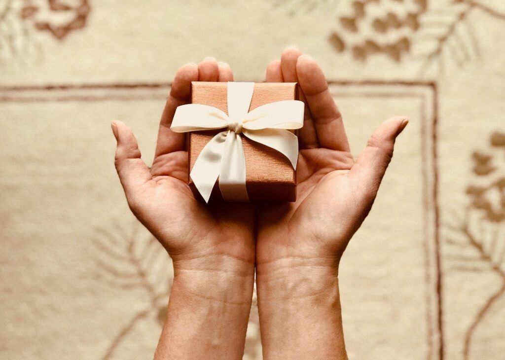 Mains ouvertes tenant un petit cadeau au ruban blanc