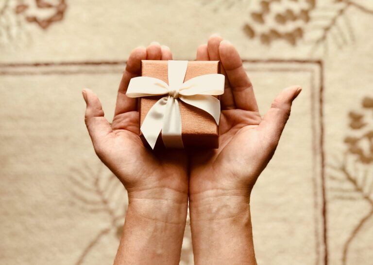 Mains ouvertes tenant un petit cadeau au ruban blanc