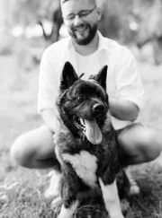 Homme souriant accroupi avec son chien noir, photo en noir et blanc