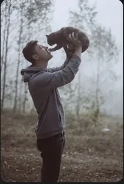 Homme soulevant joyeusement son chat dans une forêt brumeuse