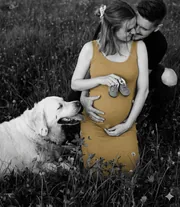 Couple attendant un bébé, assis dans l’herbe avec leur chien, photo en noir et blanc
