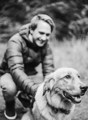 Homme accroupi souriant à côté de son golden retriever, photo en noir et blanc