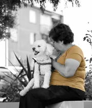Femme assise sur un banc serrant son petit chien blanc, portrait en noir et blanc