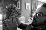 Homme à lunettes caressant son chat tigré à la maison, photo en noir et blanc