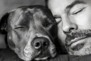 Homme et son chien les yeux fermés, joue contre joue, portrait en noir et blanc