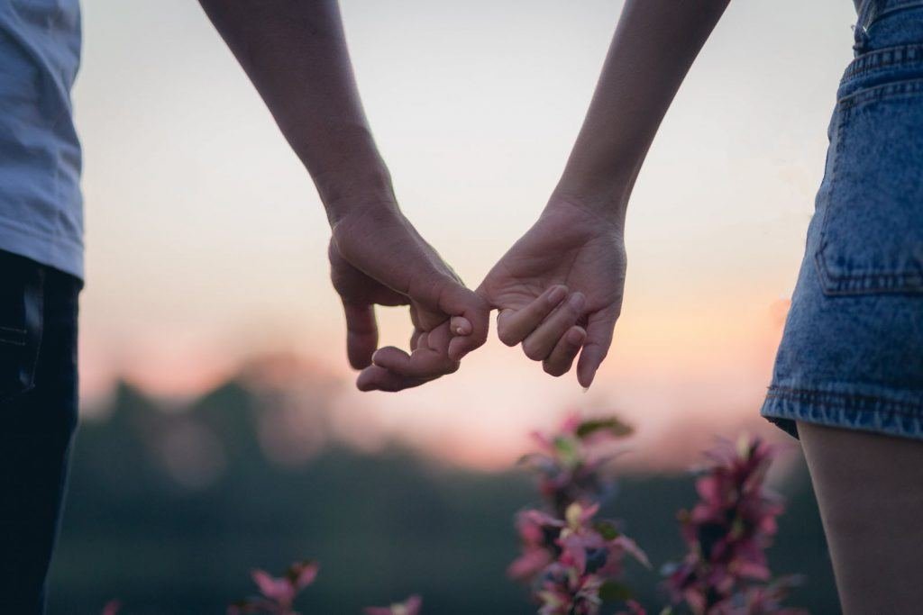 Mains d’un couple liées par le petit doigt, symbole d’une promesse d’amour