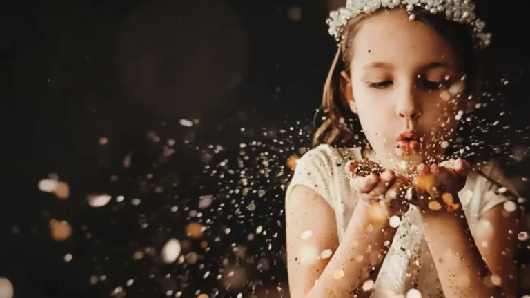 Petite fille d’honneur couronnée de fleurs soufflant des paillettes dorées dans la lumière du soir