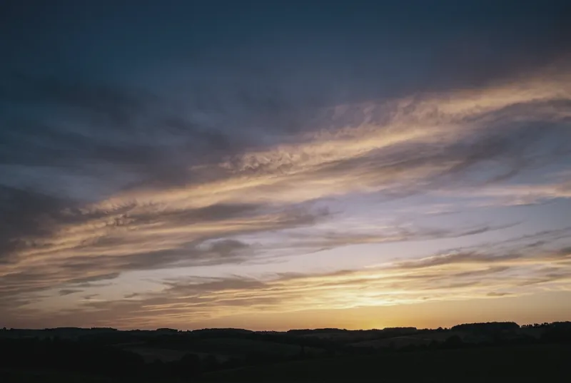 Un ciel de fin de journée aux nuages striés de lueurs dorées pâles, au-dessus de collines sombres